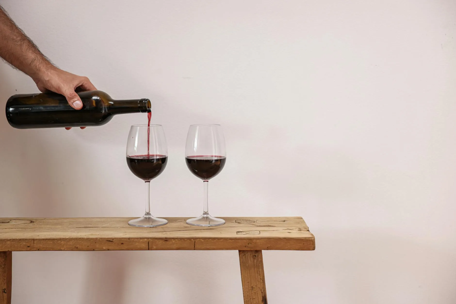 Red wine being poured from a bottle into glasses after fermentation